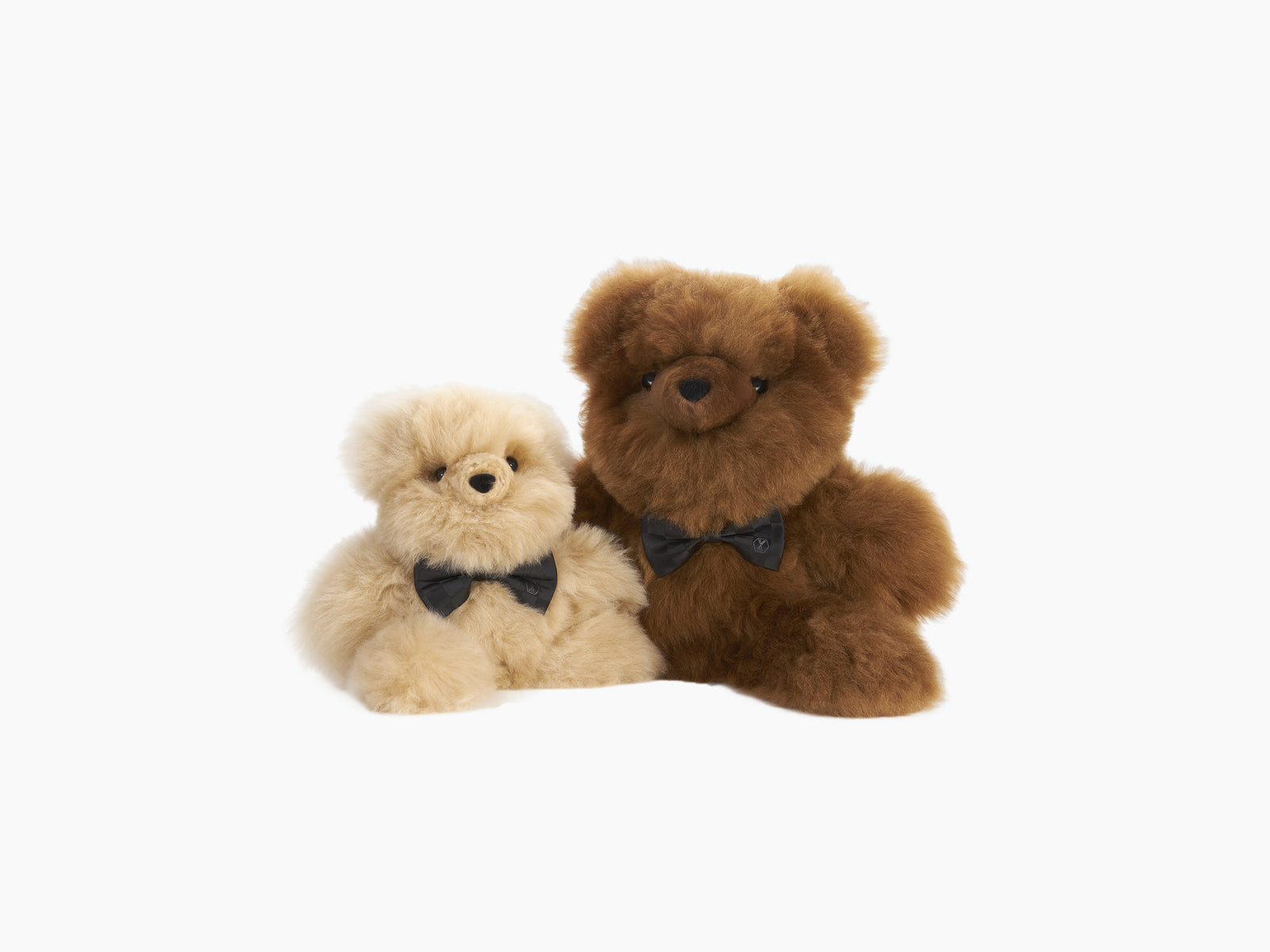 Two fluffy teddy bears in beige and brown tones with matching black bow ties.