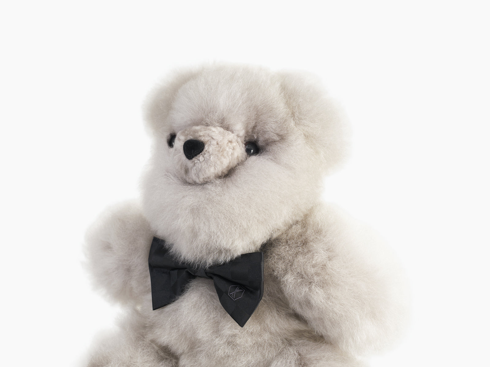 Close-up of a cream fluffy Pelu teddy bear with a black silk bow tie