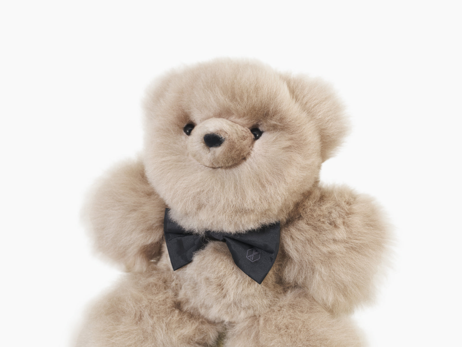 Pelu the beige teddy bear with a black silk bow tie beside a WEICH cloth bag