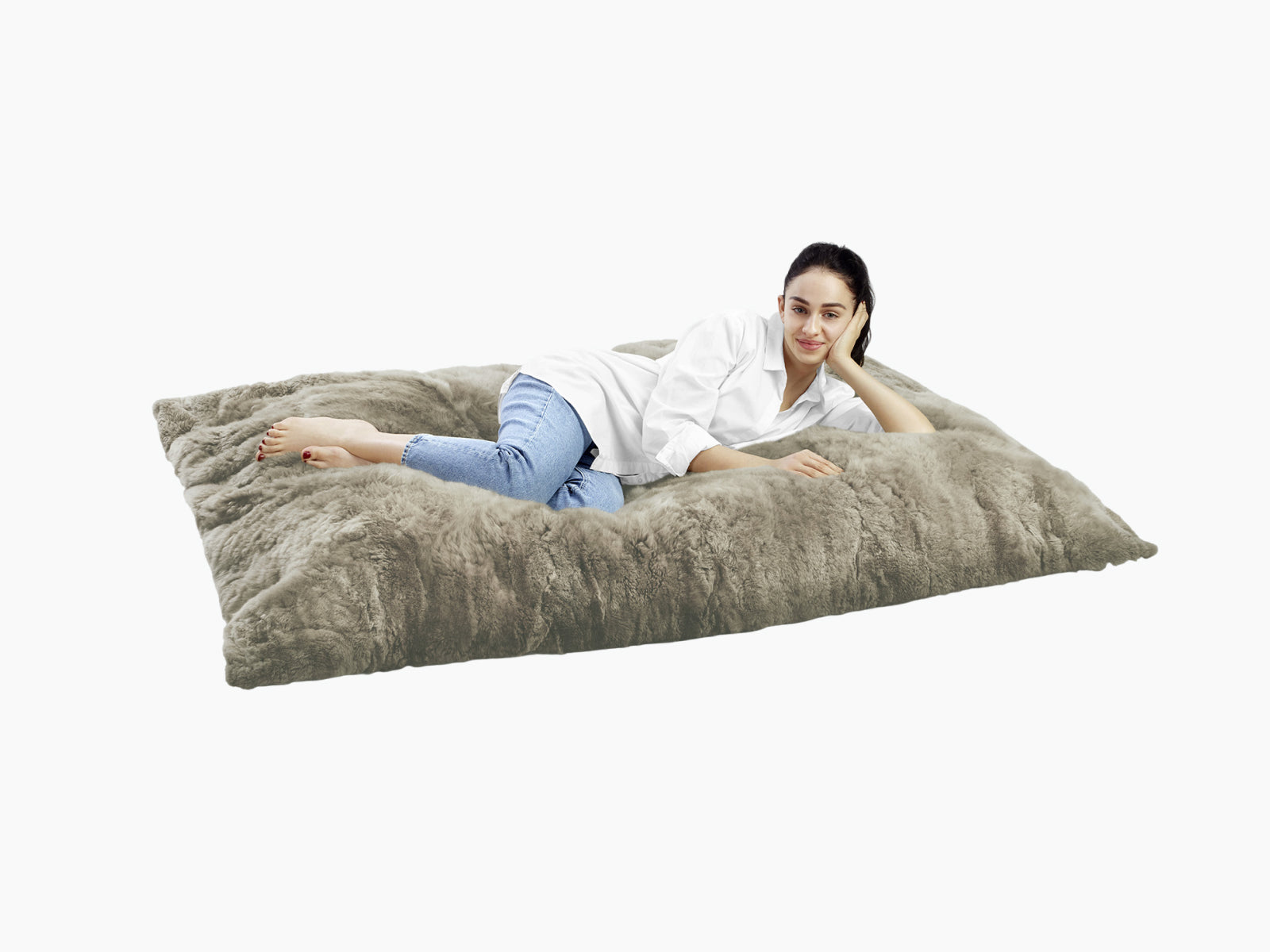 Woman lounging on a large plush fur lounger made from alpaca fur, wearing a white shirt and jeans.