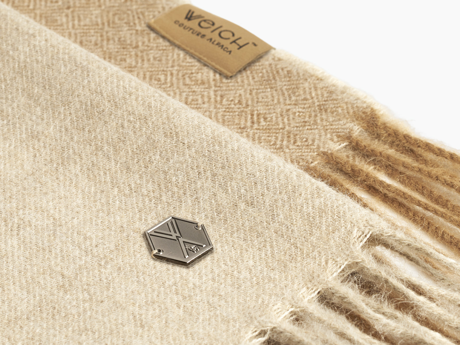 Close-up of a beige alpaca wool blanket showing fringe and a small metal tag.