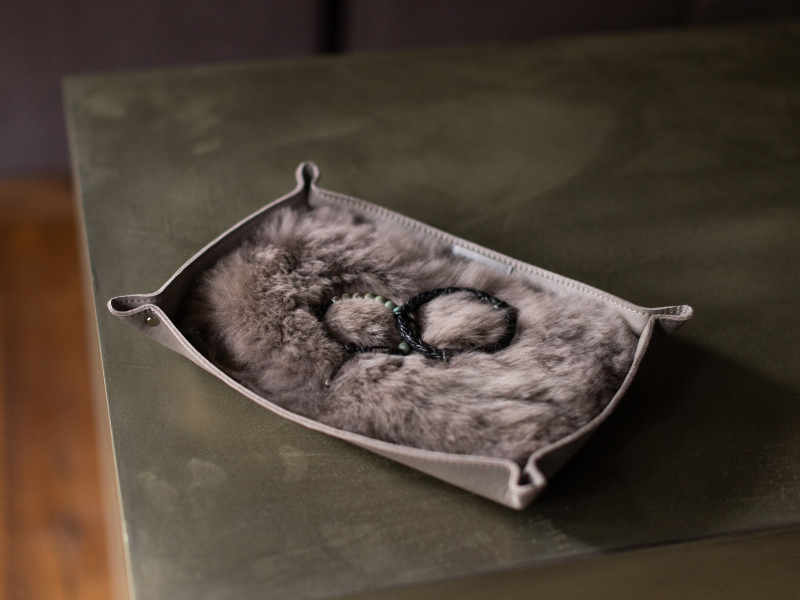 Beige leather catchall tray with plush alpaca fur interior resting on a dark table with jewelry inside