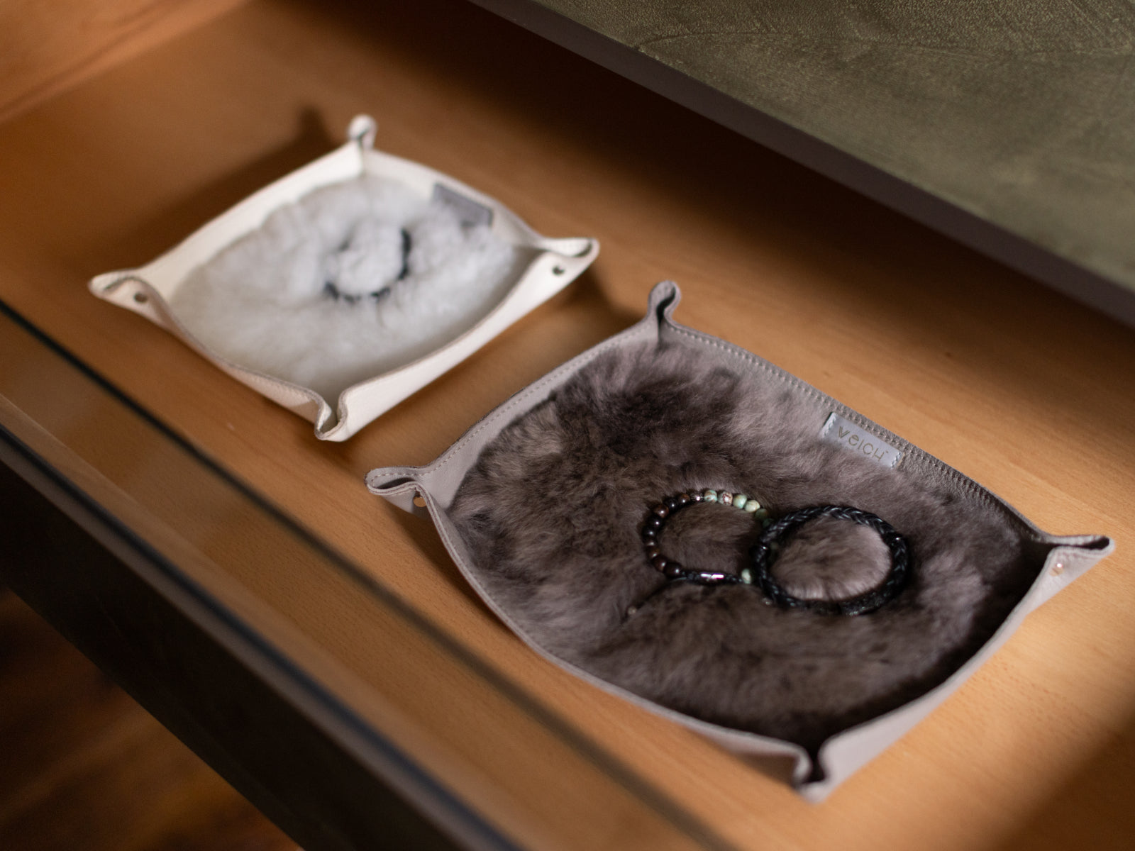 Two WEICH catchall trays with plush fur interiors on a wooden surface, one containing bracelets