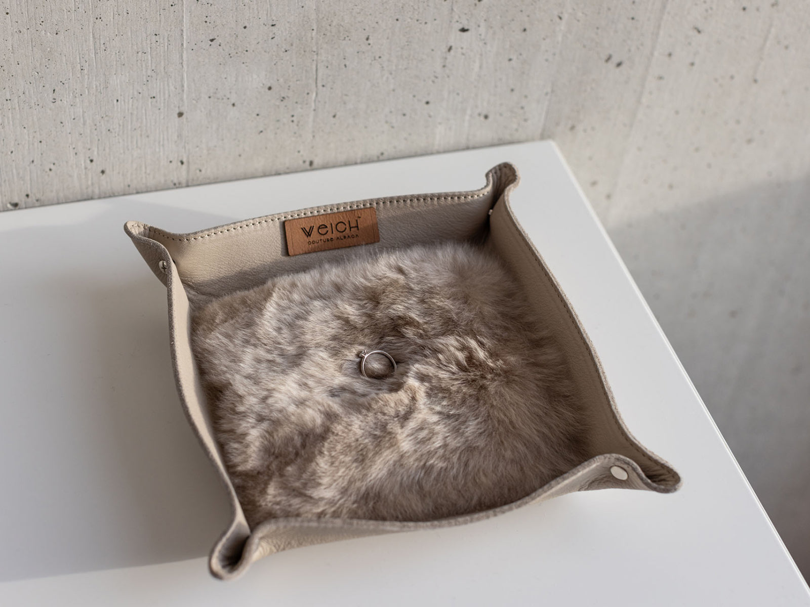 Beige leather catchall tray with plush alpaca lining and a ring resting in its center.