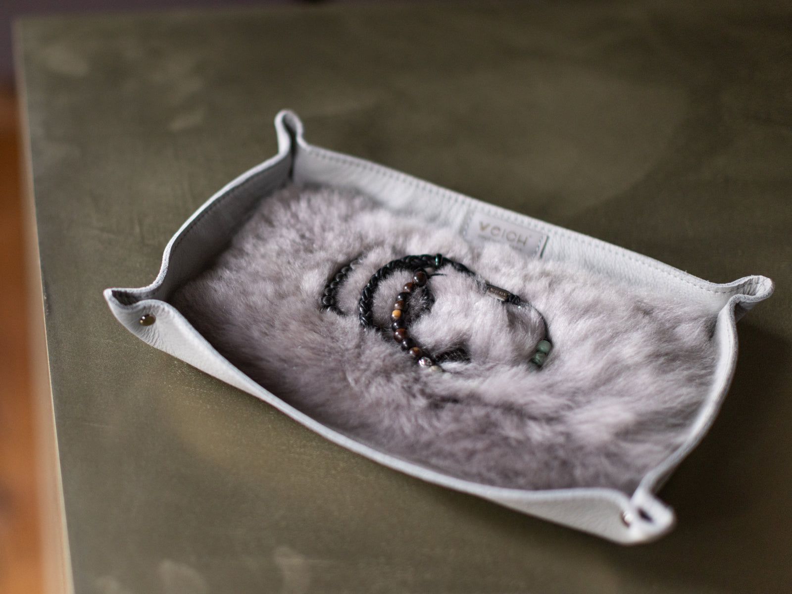 Light gray leather catchall tray with soft fur lining holding several bracelets