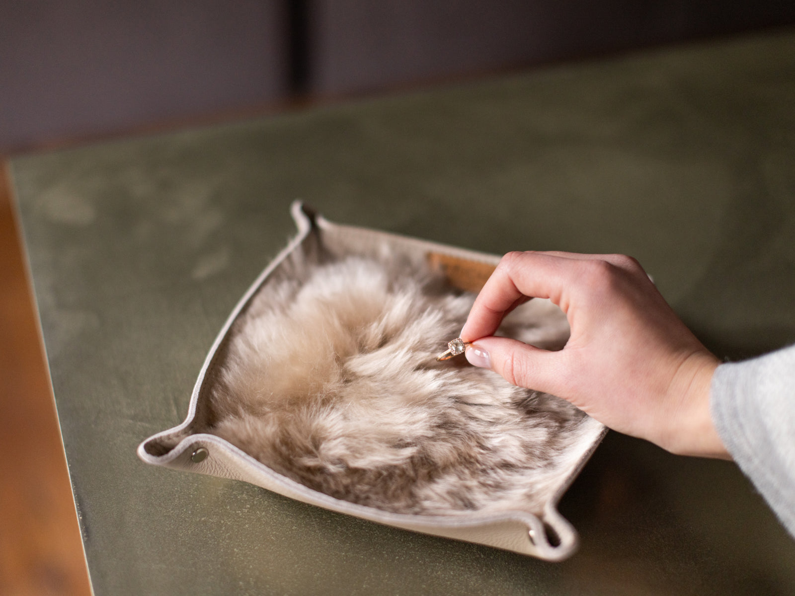 Hand places a ring into a small beige leather catchall tray with a soft alpaca lining.