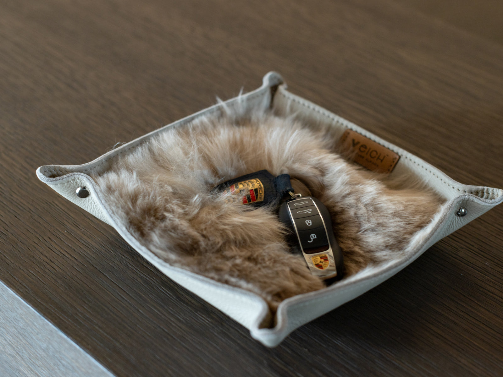 Inside view of a white WEICH catchall tray with plush fur lining and a Porsche key fob resting inside.