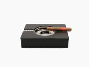 Zeno Handwoven Ashtray wrapped in black leather with a cigar resting on its chrome rim atop a black leather case